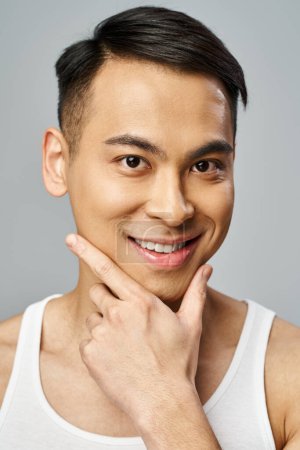 A handsome Asian man with a bright smile in a grey studio, exuding joy and contentment.