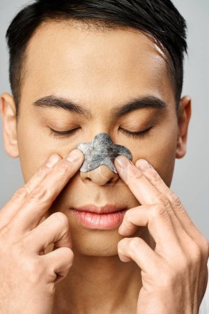 Téléchargez les photos : Un homme asiatique portant un cache-nez lors de sa routine beauté dans un studio gris. - en image libre de droit
