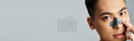 Téléchargez les photos : Portrait d'un bel homme asiatique avec une tache de nez de beauté dans un décor de studio gris. - en image libre de droit
