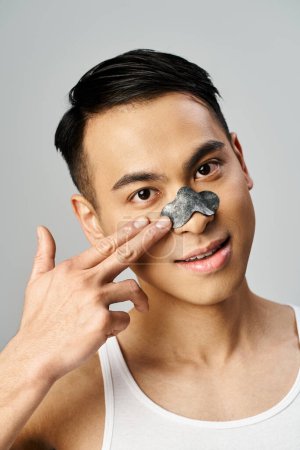 Schöner asiatischer Mann im grauen Studio trägt bei Schönheitsoperationen ein Nasenpflaster.