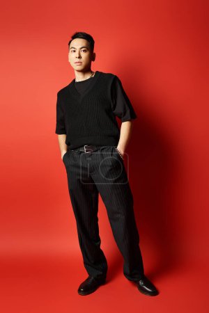 A stylish handsome Asian man stands confidently in black attire against a bold red background in a studio setting.