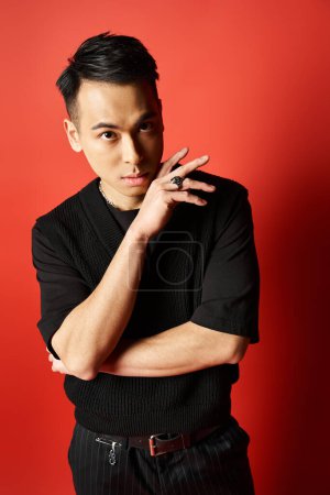 A handsome Asian man in a black shirt confidently poses for a portrait against a vibrant red background in a studio.