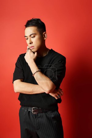 Handsome Asian man in black shirt stands confidently against vibrant red backdrop in studio setting.