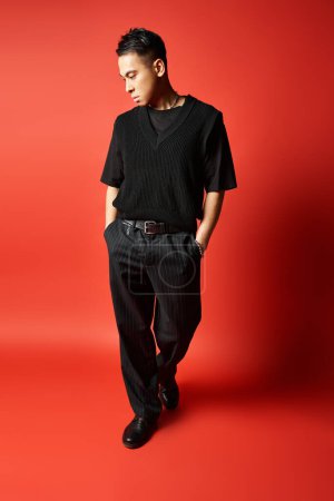 Ein stilvoller und gut aussehender asiatischer Mann in schwarzer Kleidung posiert selbstbewusst vor auffallend rotem Hintergrund in einem Studio-Setting.