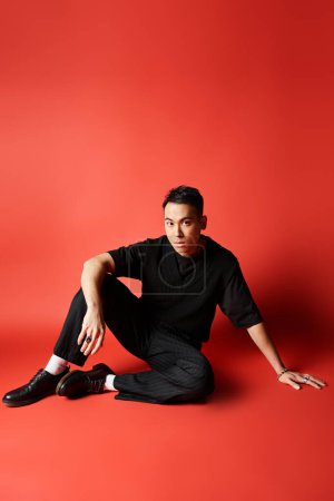 Schöner asiatischer Mann in stylischer schwarzer Kleidung sitzt mit überkreuzten Beinen auf dem Boden und strahlt Ruhe und Gelassenheit aus.