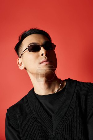 Un hombre asiático elegante y guapo con gafas de sol, posando sobre un fondo rojo vibrante.