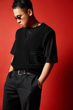 Foto de Elegante, guapo hombre asiático vestido con camisa negra y pantalones de pie con confianza en un estudio rojo. - Imagen libre de derechos