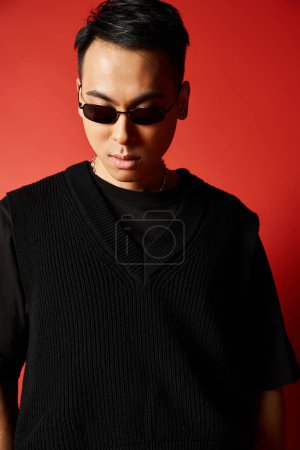 Ein stilvoller und gut aussehender asiatischer Mann mit Sonnenbrille und schwarzem Pullover vor leuchtend rotem Hintergrund.
