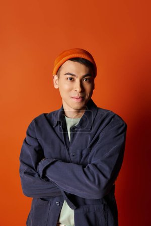 A handsome Asian man in stylish attire walks confidently against an orange backdrop.