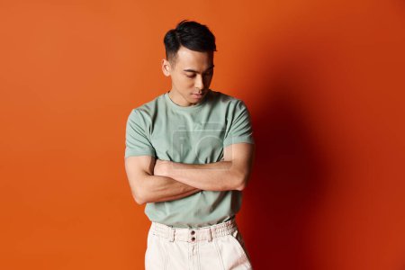 Téléchargez les photos : Un homme asiatique élégant en tenue à la mode se dresse avec confiance contre un mur orange vibrant dans un studio. - en image libre de droit