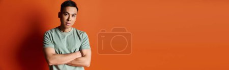 Photo for A handsome Asian man wearing stylish attire confidently stands in front of a vibrant orange wall in a studio setting. - Royalty Free Image