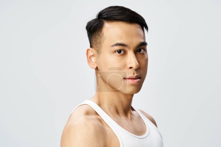 A handsome Asian man in a tank top strikes a confident pose in a grey studio setting.