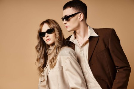 attraktives elegantes Paar in schicken saisonalen Anzügen mit stylischer Sonnenbrille posiert auf pastellfarbenem Hintergrund