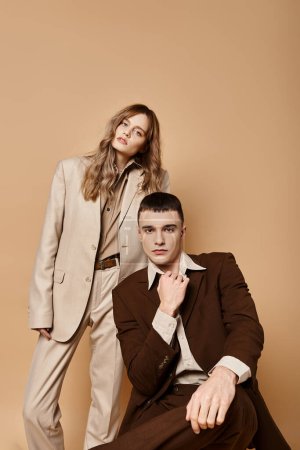 appealing couple in sophisticated suits posing together and looking at camera on pastel backdrop