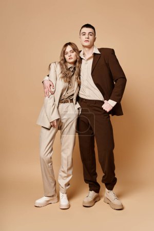 loving elegant boyfriend and girlfriend in chic suits looking at camera on pastel background