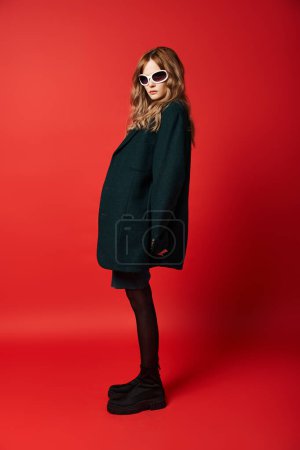 appealing fashionable woman in elegant attire with sunglasses posing on red vibrant background