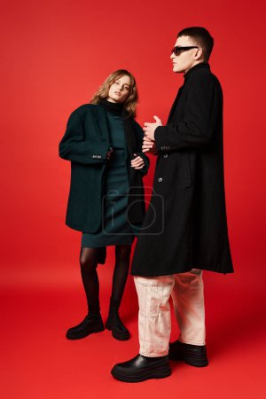 attraktive langhaarige Frau im eleganten Mantel, die in die Kamera neben ihrem Freund mit Sonnenbrille blickt