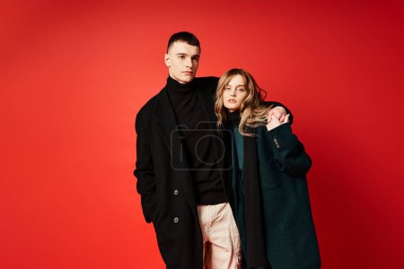 Photo for Elegant woman in coat looking at camera and posing lovingly with her boyfriend on red backdrop - Royalty Free Image