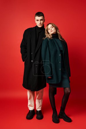 appealing loving couple in sophisticated coats looking at camera on red vibrant background