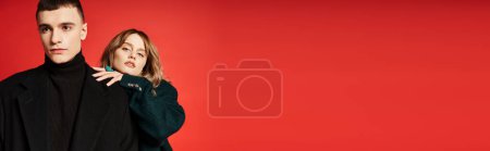 chic pretty woman looking at camera and posing lovingly with her boyfriend on red backdrop, banner