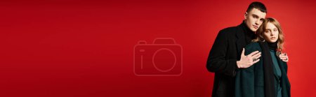 young loving couple in sophisticated coats looking at camera on red vibrant background, banner