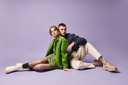 Téléchargez les photos : Belle femme élégante en veste verte assise sur le sol avec son petit ami et regardant la caméra - en image libre de droit