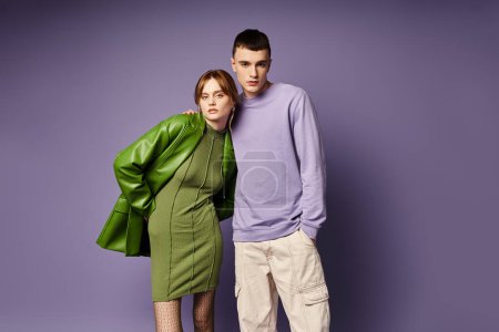 Téléchargez les photos : Couple bien habillé en vêtements vibrants posant ensemble sur fond violet et regardant la caméra - en image libre de droit