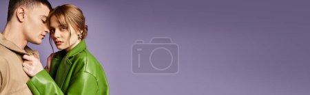 stylish woman in green jacket looking at camera near her loving boyfriend on purple backdrop, banner