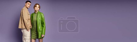 Téléchargez les photos : Couple aimant élégant dans des vêtements vibrants posant ensemble sur fond violet et regardant la caméra - en image libre de droit