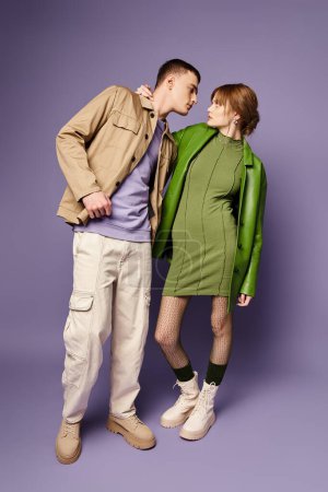 Téléchargez les photos : Séduisant couple aimant dans des vêtements colorés vibrants en regardant les uns les autres sur fond violet - en image libre de droit