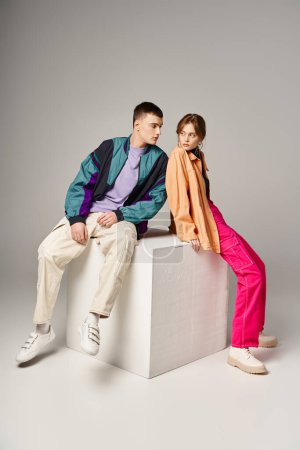 young appealing couple in vibrant trendy bombers looking at each other lovingly on white cube