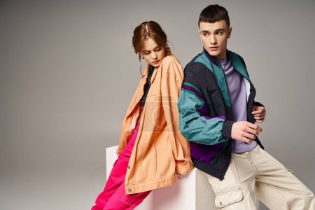 stylish good looking couple in vibrant everyday clothes looking away on gray backdrop on white cube