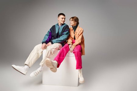 Téléchargez les photos : Joyeux couple attrayant dans vibrant bombardiers à la mode se regardant joyeusement sur cube blanc - en image libre de droit