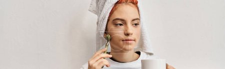 Photo for Appealing queer person with hair towel using face roller and holding tea cup while at home, banner - Royalty Free Image