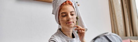 Photo for Beautiful queer person in homewear using face roller in front of mirror as morning routine, banner - Royalty Free Image