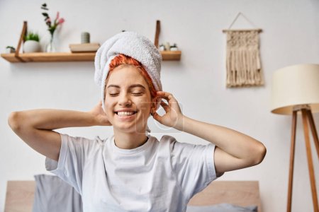 Photo for Cheerful extravagant person with white hair towel sitting on her bed at home, morning routine - Royalty Free Image