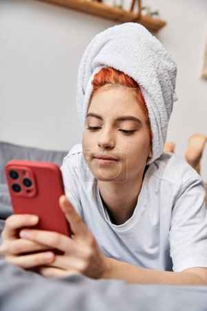 appealing extravagant person with white hair towel looking at her phone while relaxing in bed
