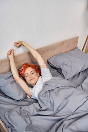 Photo for Extravagant pretty queer person in casual attire waking up and stretching in her bed, leisure time - Royalty Free Image