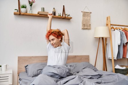 extravagant young queer person in casual attire waking up and stretching in her bed, leisure time