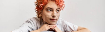 relaxing red haired queer person sitting on her bed at home and looking away, leisure time, banner