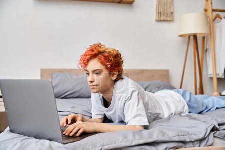 joyous appealing queer person in cozy homewear lying in bed and surfing in internet, leisure