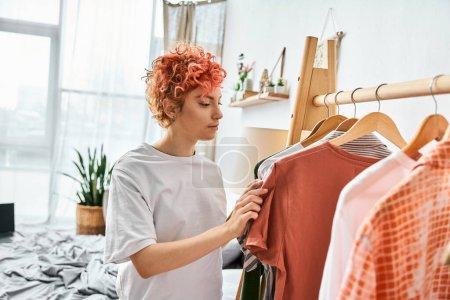 Photo for Attractive red haired extravagant person picking up stylish clothes near rack at home, leisure time - Royalty Free Image