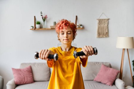 Photo for Appealing young queer person in vibrant sport attire exercising with dumbbells while at home - Royalty Free Image