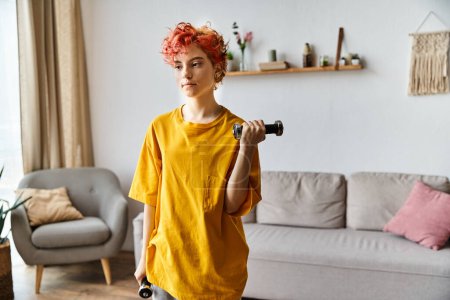 Photo for Attractive young queer person in vibrant sport attire exercising with dumbbells while at home - Royalty Free Image