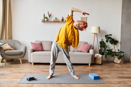 Photo for Good looking jolly queer person in casual attire exercising actively on yoga mat while at home - Royalty Free Image