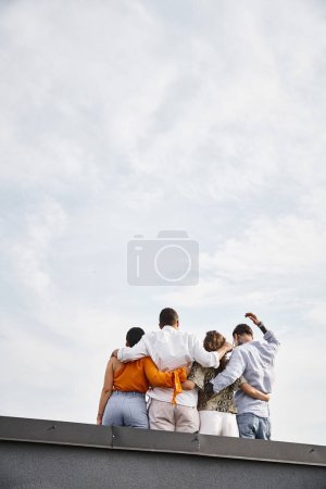 Rückansicht einer Gruppe junger multikultureller Freunde in lässiger urbaner Kleidung, die auf dem Dach posieren
