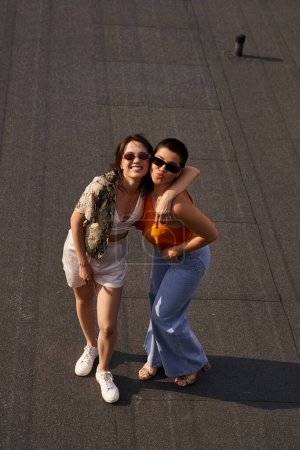 freudig schöne Frauen in lebhaften Freizeitanzügen posieren gemeinsam auf dem Dach und lächeln in die Kamera