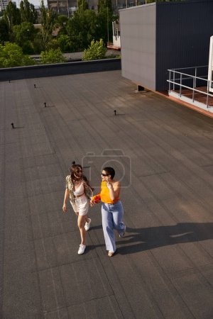 zwei lustige schöne junge Frauen in lässiger Kleidung mit Sonnenbrille posieren gemeinsam auf dem Dach