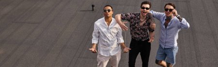 interracial jolly male friends with sunglasses posing on rooftop and looking at camera, banner