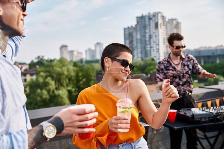 cheerful friends in casual attires with sunglasses drinking at rooftop party and dancing to DJ set